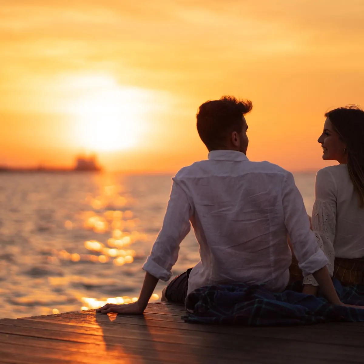 Paar sitzt bei Sonnenuntergang am Meer, von hinten