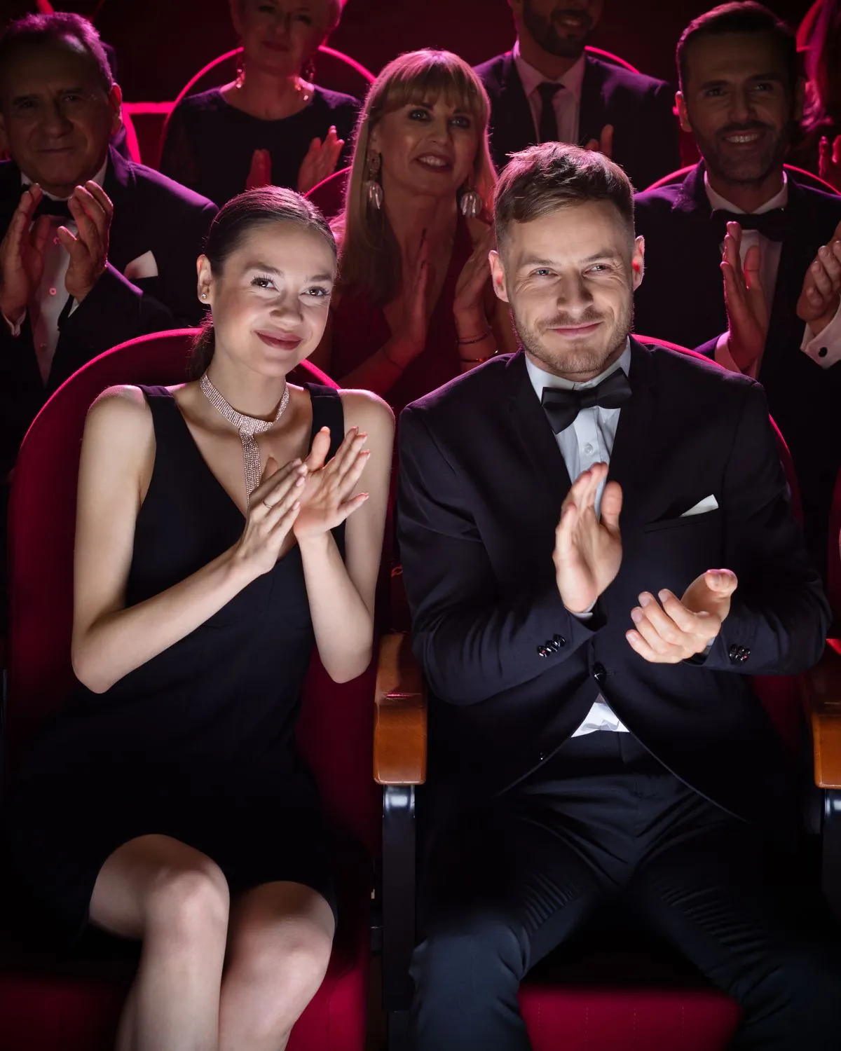 Elegant gekleidetes Paar applaudiert im Theater, dahinter weiteres Publikum