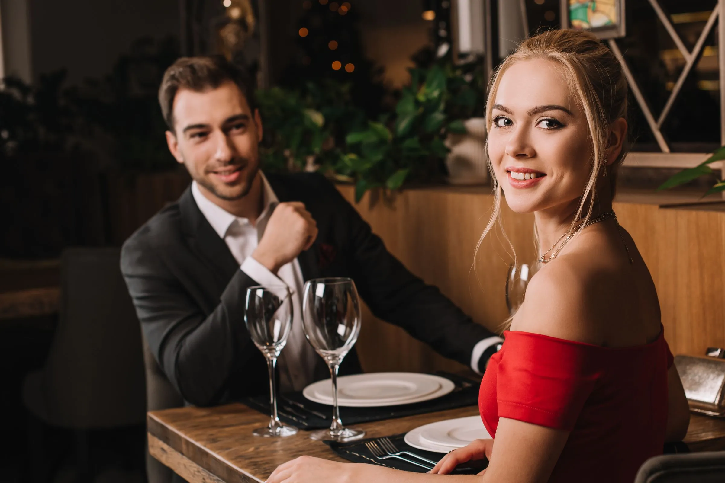 Paar am gedeckten Tisch in einem Restaurant, die Frau im roten Kleid lächelt über die Schulter