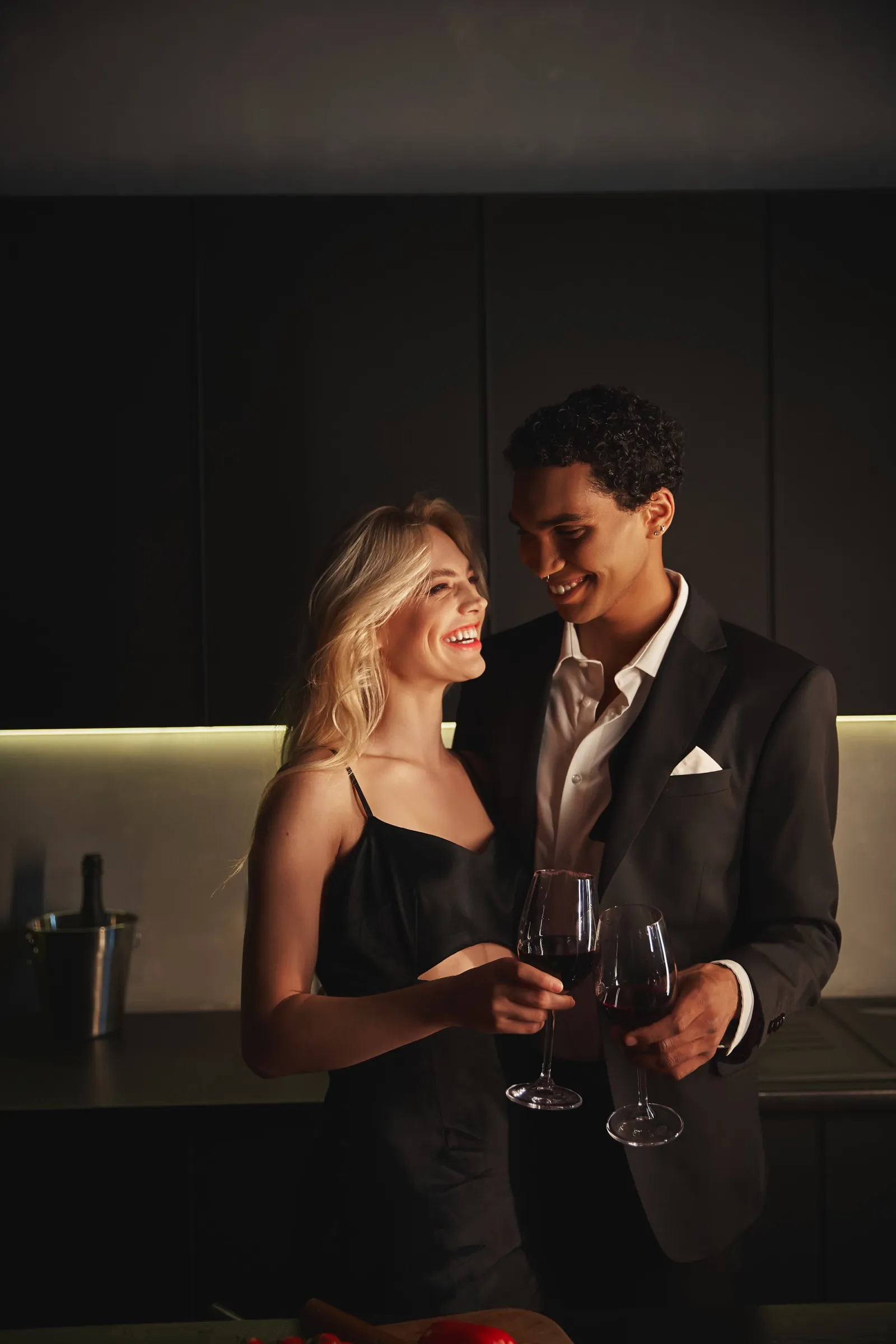 Elegantes Paar stößt am Abend mit Rotwein in einer dunklen, modernen Küche an